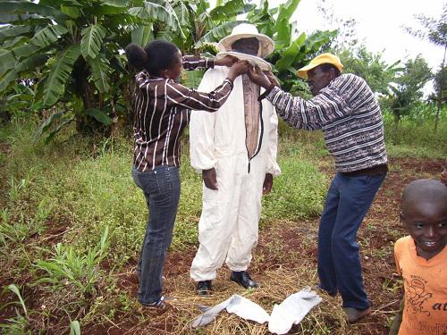 A beekeeper being shown how to wear a new bee suit.